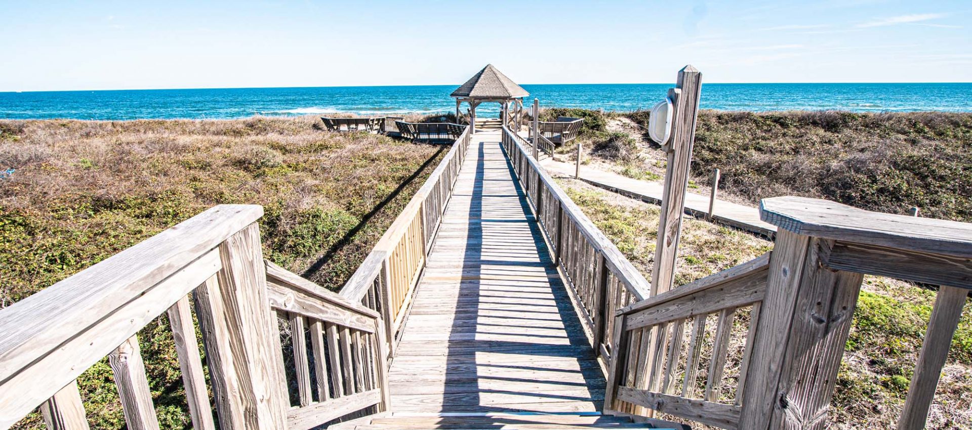 Photo of pathway from resort to the beach with gazebo at the end, showcasing the ocean in the back.